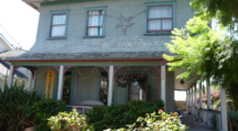 Frontal view of the Vawter House, a two-story residential home with three windows visible on the top floor, two windows visible on the bottom floor and a doorway. The porch is located on the right side of the house. Shrubbery surrounds the front of the house on the lower left of the image.