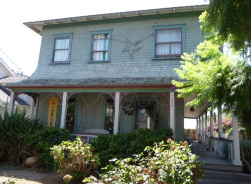 Frontal view of the Vawter House, a two-story residential home with three windows visible on the top floor, two windows visible on the bottom floor and a doorway. The porch is located on the right side of the house. Shrubbery surrounds the front of the house on the lower left of the image.