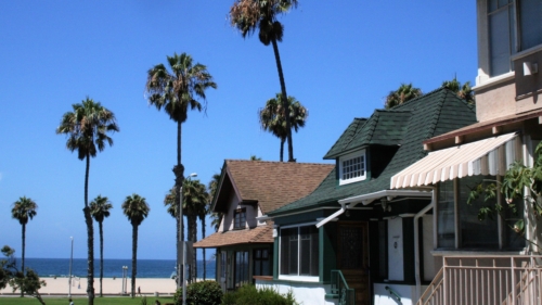  Three modest two-story homes in an eclectic mix of early 20th century residential styles frame a view of palm trees, sand and the ocean beyond. 