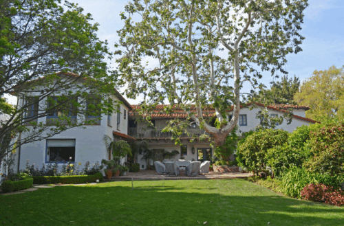  The Armstrong-Cobb residence seen across backyard of a large two-story Spanish Colonial revival home with a 2nd story verandah and patio behind a green lawn and two large mature trees.