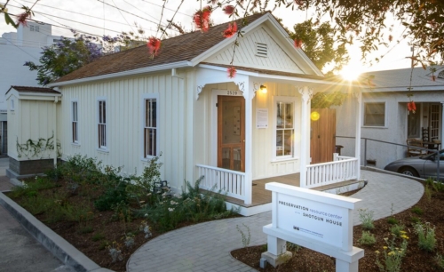  The front and side elevations of the restored shotgun house with surrounding native plant garden and front sign reading, preservation resource center at the shotgun house.