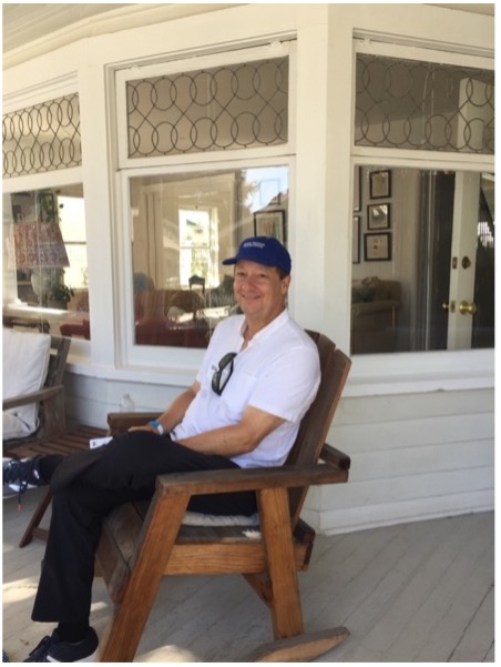 Alec on a visit to a historic site, sitting on a rocking chair with a Santa Monica Conservancy hat.